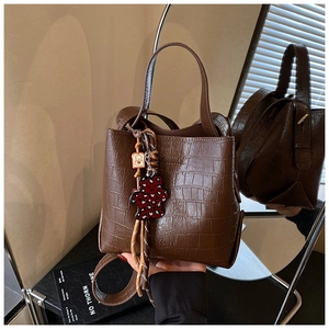 Detail of dark brown crocodile pattern bucket bag with a cute bear charm and shoulder strap