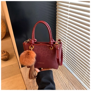 Détail d'un sac seau bordeaux à relief léopard avec ferrures dorées et pompon en fourrure