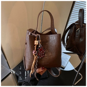 Macro shot of dark brown crocodile texture bucket bag with leopard bear charm and brand logo