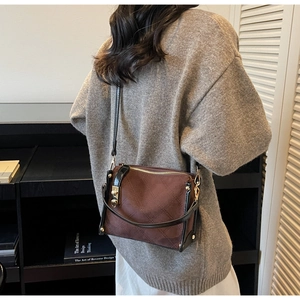 Detail of a brown quilted crossbody bag with black leather trim and golden metal lock