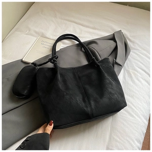 Close-up of black tote bag with small round pouch on a grey blazer and magazine