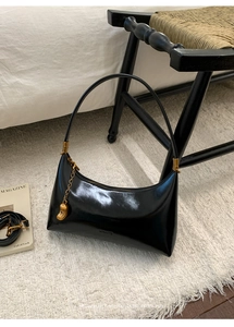 Detail of glossy black hobo bag with vintage gold hardware and metal charm on white rug