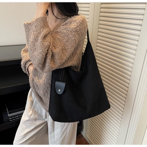 Detail of a large black tote bag with matte texture and leather charm on the side