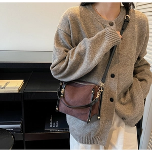 Detail of brown suede crossbody bag with black trim and gold hardware in a lifestyle setting