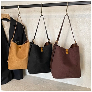 Close-up of three suede tote bags in yellow, black, and brown with vintage metal buckles