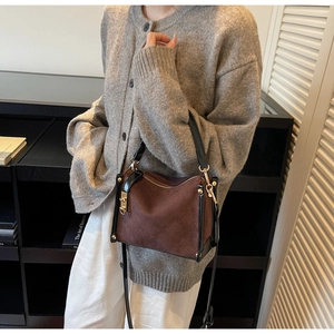 Detail of a brown quilted square crossbody bag with black trim and gold clasp lock