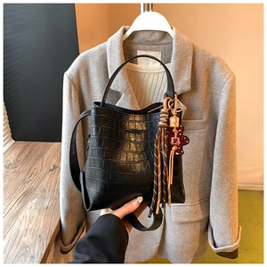 Detail of black crocodile texture bucket bag with fringe and bear charm on wood