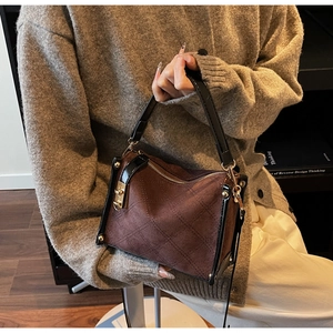 Detail of dark brown suede handbag with quilted stitching and gold hardware buckle