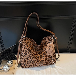 Detail of leopard print tote bag with brown straps and plush dog charm on white desk