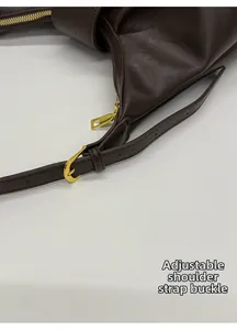 Detail of dark brown leather handbag with adjustable gold buckle strap and sleek hardware
