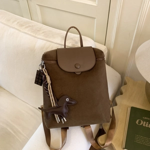 Close-up of a brown nylon backpack with leather flap and cute dachshund charm on a sofa