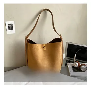 Detail of ginger suede bucket bag featuring a golden square lock and leather shoulder strap
