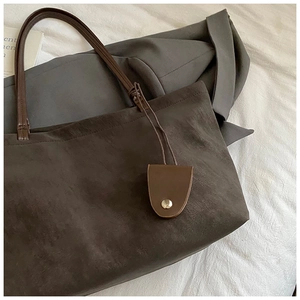 Detailed view of dark brown suede tote bag with leather strap and small golden button pouch