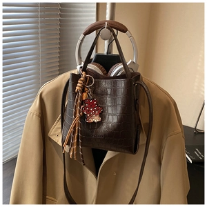 Detail of dark brown crocodile bucket bag with leopard bear charm and striped tassel