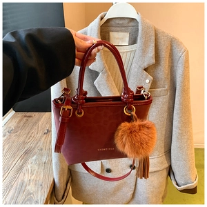 Gros plan sur un sac seau bordeaux en cuir avec poignées, bandoulière et pendentif à pompon