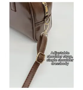 Detail of dark brown tote bag showing gold zipper, metal buckle and adjustable strap