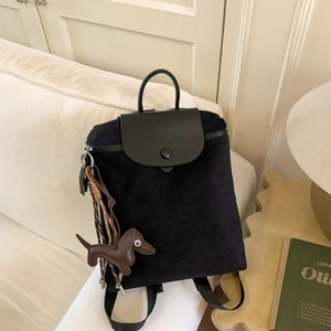 Detail of black nylon travel backpack featuring a leather flap and brown dog keychain