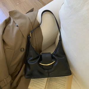 Detail of black leather hobo bag with gold metal buckle resting on a trench coat