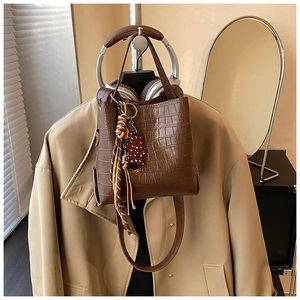 Detail of dark brown crocodile embossed bucket bag with bear charm and striped handle scarf