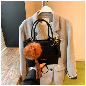 Détail d'un sac à main léopard noir avec pompon orange et finitions dorées élégantes