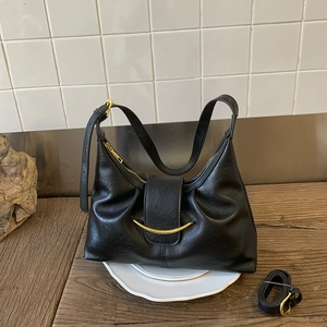 Detail of black semi-moon hobo bag with gold hardware on white ceramic plate