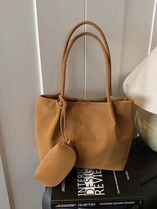 Large caramel faux leather tote bag with inner pouch on a minimalist bookshelf setup