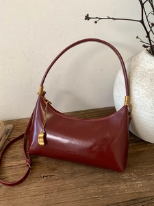 Vintage burgundy leather baguette shoulder bag with metal chain detail on wooden table
