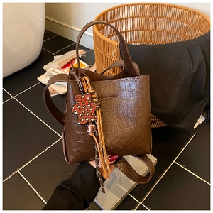 Detailed close-up of dark brown crocodile-embossed leather bucket bag with bear charm