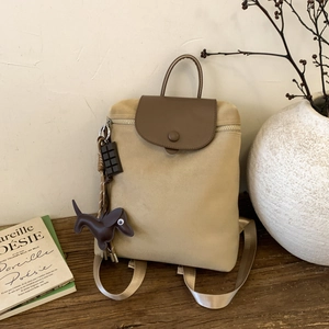 Beige canvas and brown leather minimalist backpack with chic dog charm on a wooden table
