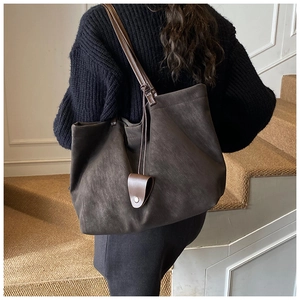 Detail of dark brown suede tote bag featuring a minimalist strap and leather charm