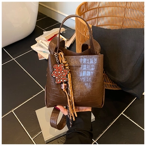 Detail of brown croc-effect bucket bag with leopard bear charm and woven tassel detail