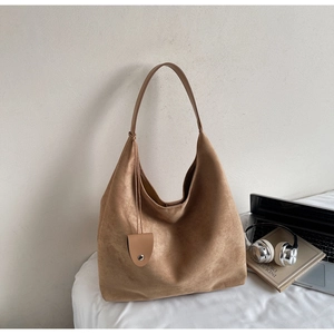 Detailed close-up of a camel suede hobo tote bag placed next to industrial design books