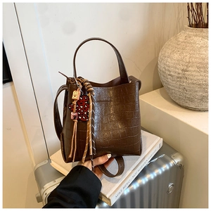 Detailed view of dark brown crocodile-embossed bucket bag with chic leopard heart charm