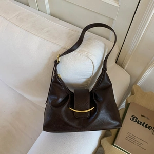 Close-up of a dark brown leather hobo bag with a gold metal accent on an off-white sofa