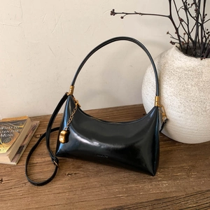 Detailed view of black patent leather hobo bag with gold chain on a wooden table
