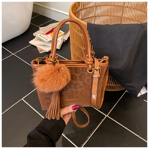 Gros plan du sac seau marron en daim léopard avec pompon en peluche et logo doré