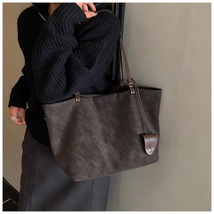 Detail of dark brown tote bag showing textured matte leather and metal rivet tag
