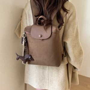 Detail view of a vintage brown canvas backpack with leather accents and dog charm accessory
