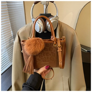 Détail d'un sac seau marron à imprimé léopard avec pompon en peluche et glands