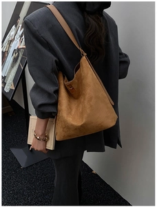 Detail view of large tan suede bucket bag with metallic buckle on a grey suit model
