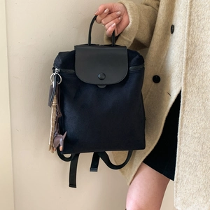 Detailed view of the black nylon backpack featuring leather flap and horse charm