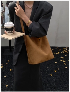 Close-up of brown suede bucket bag with gold clasp shown on model with autumn styling