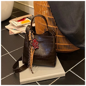 Detail of dark brown crocodile pattern bucket bag with red leopard bear charm decoration