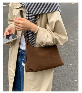Close-up of a brown suede crescent bag worn with a beige trench coat and scarf