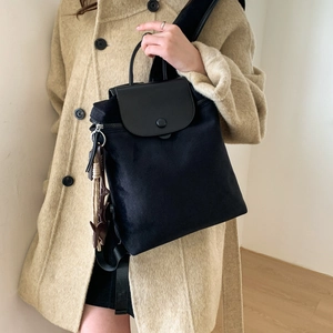 Detail of nylon backpack featuring a black leather flap, snap button closure and top handle