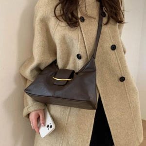 Detailed view of the dark brown dumpling bag with a crescent gold buckle on a beige coat