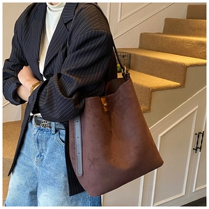 Detail of dark brown suede bucket bag with adjustable strap and metal hardware