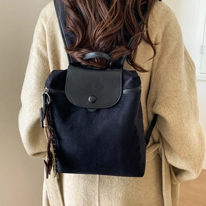 Detailed side view of black nylon backpack featuring leather flap and button closure