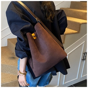 Detail of a brown suede bucket bag with leather strap and gold metal twist lock