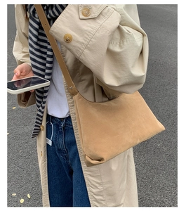 Close-up of camel suede hobo bag worn with a trench coat and casual jeans